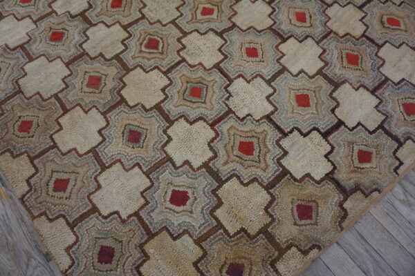 A rustic, heavily textured rug featuring beige and red geometric motifs on gray wood flooring.