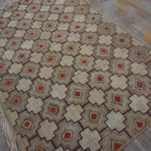 Beige textured rug with repeating red and brown geometric motifs lies on distressed gray wood flooring.