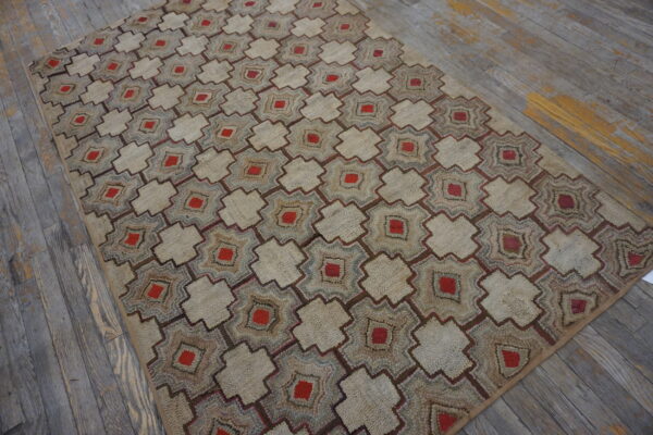 Beige textured rug with repeating red and brown geometric motifs lies on distressed gray wood flooring.