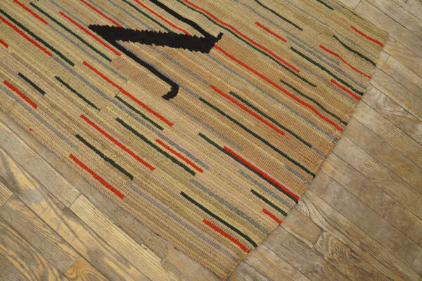 Textured beige rug with short red, gray, and dark green stripes, featuring a large black angular shape on wood planks.