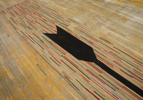 Textured runner rug with beige ground, multicolored dash stripes, and a large black arrow on wood.