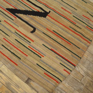 Beige textured rug with colorful dashes and a black motif lies diagonally on distressed wooden flooring.