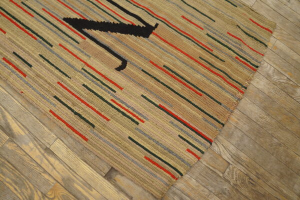 Beige textured rug with colorful dashes and a black motif lies diagonally on distressed wooden flooring.