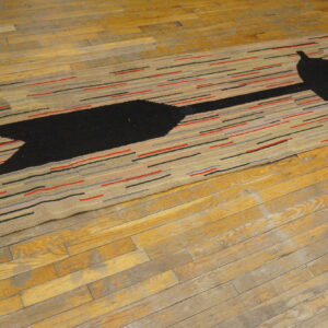 Low-pile rug with a black arrow design and colorful horizontal dashes covers worn wood flooring.