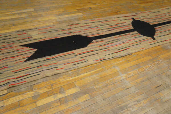 Low-pile rug with a black arrow design and colorful horizontal dashes covers worn wood flooring.