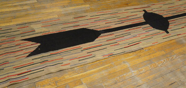 Textured beige runner rug featuring a large black arrow design and multicolored horizontal stripes on hardwood flooring.