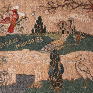 Textured folk art rug in tan, forest green, and red depicting a landscape with birds, a house, and trees.