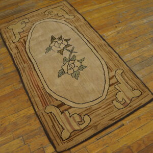 Tan hooked rug with central floral oval and striped brown border, resting on worn hardwood flooring.