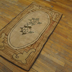 Beige hooked rug runner featuring an oval rose medallion and stylized brown motifs, set on worn wood floors.