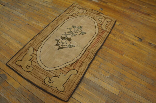 Beige hooked rug runner featuring an oval rose medallion and stylized brown motifs, set on worn wood floors.