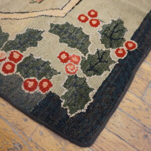 Hooked rug corner featuring green holly and red berries rests on distressed hardwood planks.