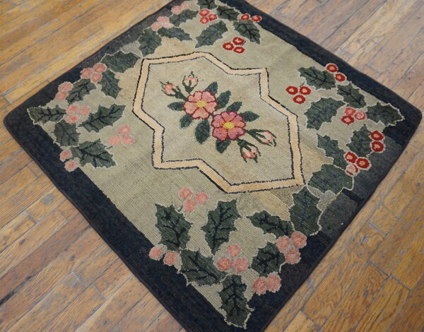 Low-pile square rug displaying a pink and red floral design framed by green leaves on rustic wood floors.