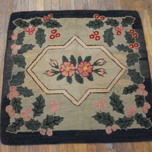 Hooked rug with green and khaki ground featuring a central floral medallion and berry wreath border on wood floors.