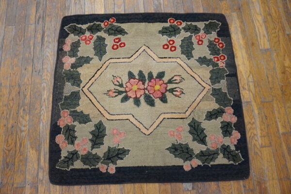 Hooked rug with green and khaki ground featuring a central floral medallion and berry wreath border on wood floors.