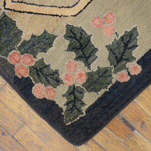 Hooked rug corner showing green holly and pink berries on a khaki field over worn wood flooring.