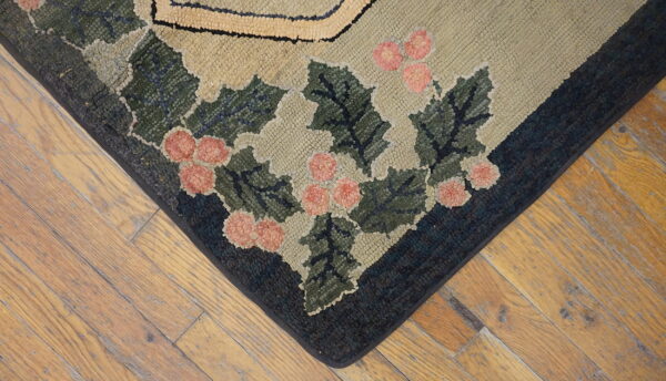 Hooked rug corner showing green holly and pink berries on a khaki field over worn wood flooring.