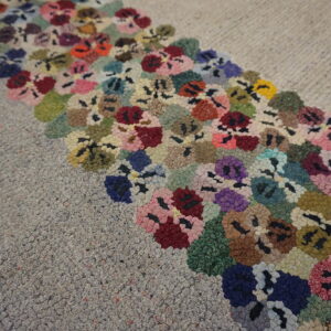 A gray loop pile rug with a wide band of colorful floral hooks rests on light wood flooring.