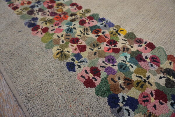 A gray loop pile rug with a wide band of colorful floral hooks rests on light wood flooring.