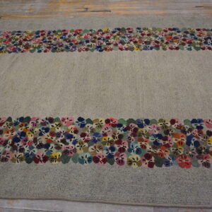 Textured gray rug with a multicolor floral border surrounding the field, placed on wood floor.
