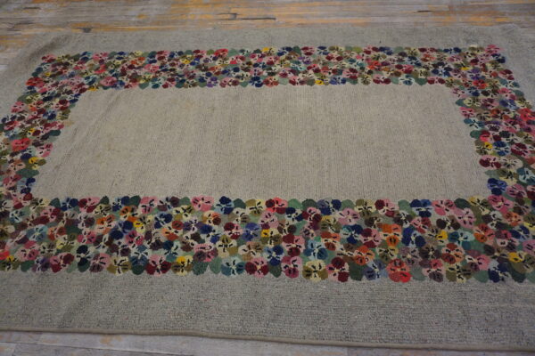 Textured gray rug with a multicolor floral border surrounding the field, placed on wood floor.