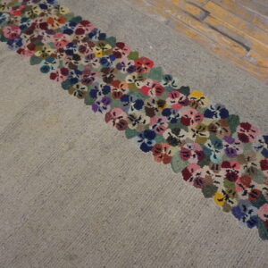 Textured beige rug featuring a wide border of densely packed, multicolored floral motifs on distressed wood.