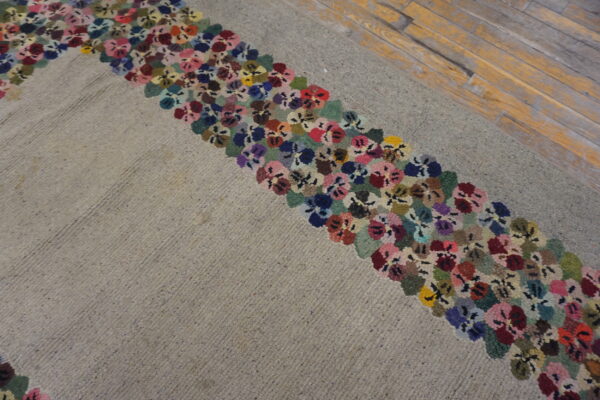 Textured beige rug featuring a wide border of densely packed, multicolored floral motifs on distressed wood.