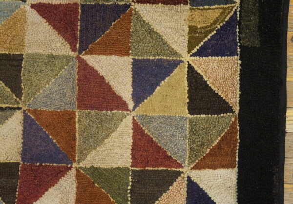 Close up of a hooked rug featuring multicolored geometric triangles and a solid black border.