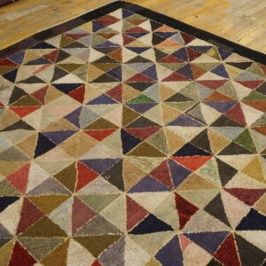 Textured multi-color rug with a dense triangular geometric pattern and dark border on a wood floor.