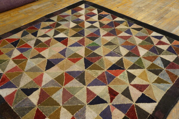 Textured multi-color rug with a dense triangular geometric pattern and dark border on a wood floor.