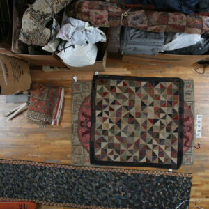 Multi-colored geometric square rug and dark abstract runner lie on a cluttered hardwood floor.