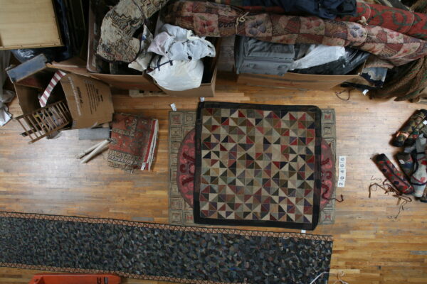 Multi-colored geometric square rug and dark abstract runner lie on a cluttered hardwood floor.