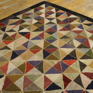 Rug with a dense geometric pattern of variegated multicolored triangles rests on a light hardwood floor.