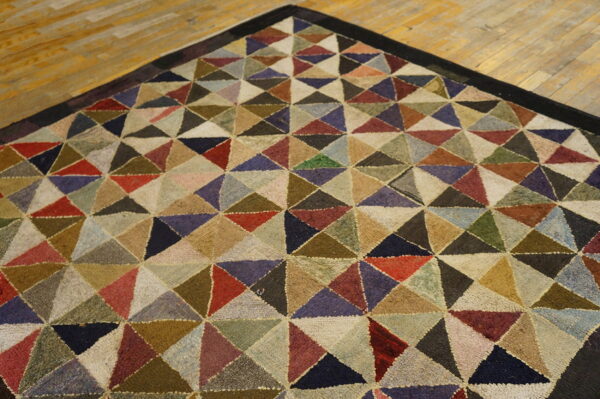 Rug with a dense geometric pattern of variegated multicolored triangles rests on a light hardwood floor.