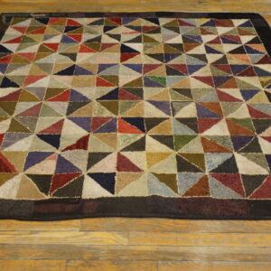 Muted multicolored rug with a looped triangular patchwork design and a solid dark border on hardwood.