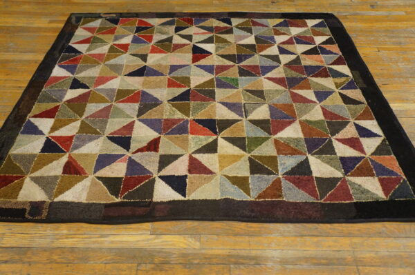 Muted multicolored rug with a looped triangular patchwork design and a solid dark border on hardwood.