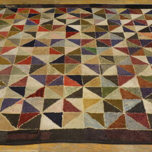 Multicolor geometric rug featuring varied triangular blocks, a dark border, and a chunky pile texture on wood flooring.