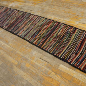 Very long, narrow multicolor strip-patterned braided runner on a distressed wood floor.