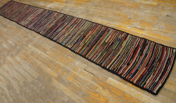Very long, narrow multicolor strip-patterned braided runner on a distressed wood floor.