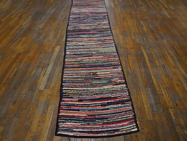 A narrow, multicolor striped runner with dark edges lies lengthwise on distressed brown wood planks.