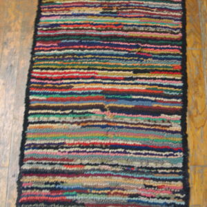 Narrow runner rug featuring chunky multicolored horizontal stripes placed on light brown wood planks.