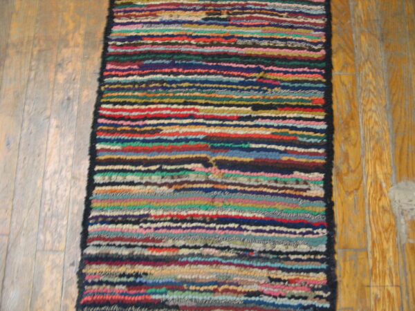 Narrow runner rug featuring chunky multicolored horizontal stripes placed on light brown wood planks.