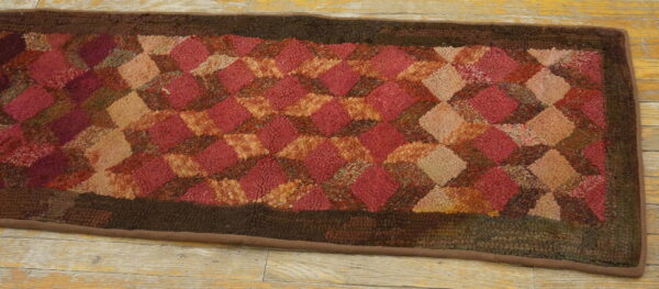 Textured runner rug with a tumbling diamond pattern in mixed reds, rust, and tan, framed by dark brown.