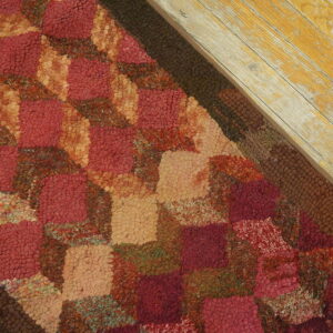 A deep red and tan block-patterned hooked rug sits next to highly distressed yellow floorboards.