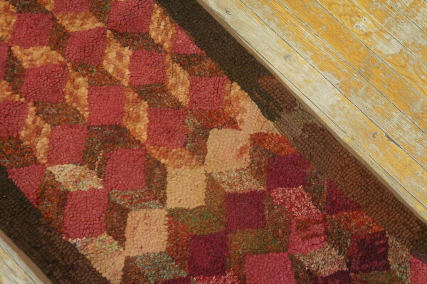A deep red and tan block-patterned hooked rug sits next to highly distressed yellow floorboards.