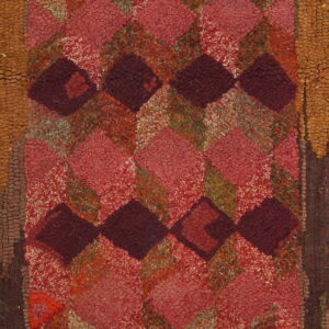 Heavily textured rug featuring a geometric diamond pattern in reds, burgundy, and earth tones against light wood.