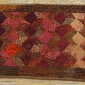 Looped pile rug with a variegated diamond pattern in deep reds, pinks, tans, and dark brown borders on wood flooring.