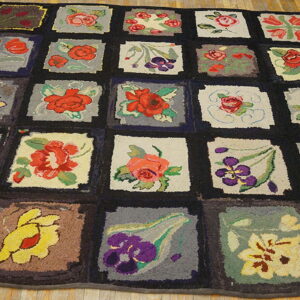 A dark-bordered quilt-style rug with multicolored floral and bird squares resting on light wood floors.