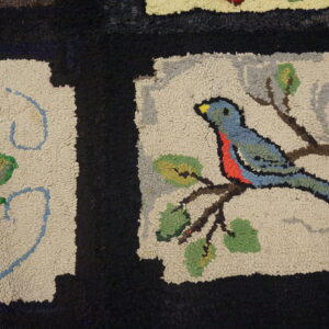 Textured rug shows motifs of a red rose and a blue bird on cream panels with thick black bands.