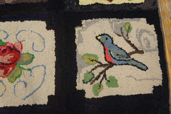 Textured rug shows motifs of a red rose and a blue bird on cream panels with thick black bands.