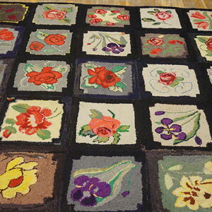 Hooked rug with a colorful grid pattern of various floral motifs resting on distressed wood flooring.